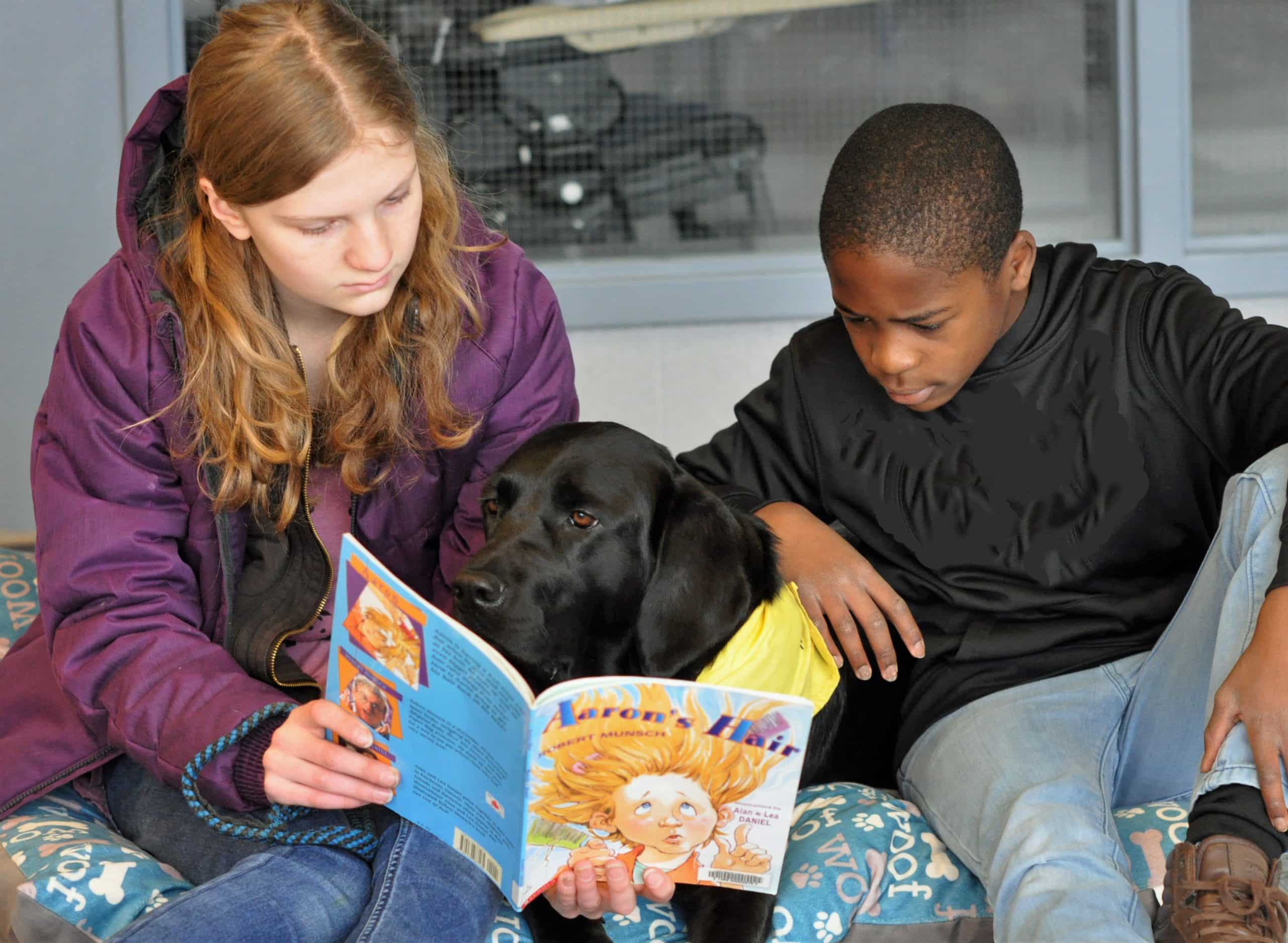 two students reading a book to a cope dog